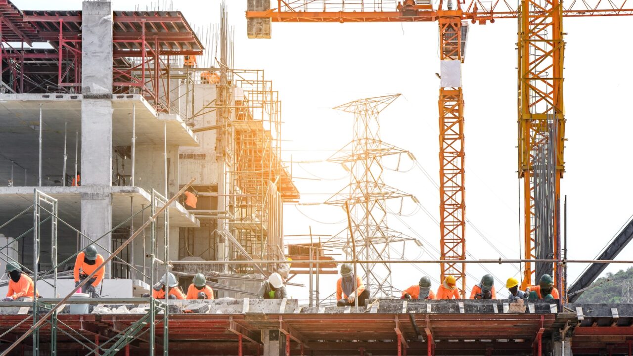 Industrial employees working on a large construction site with several large cranes.