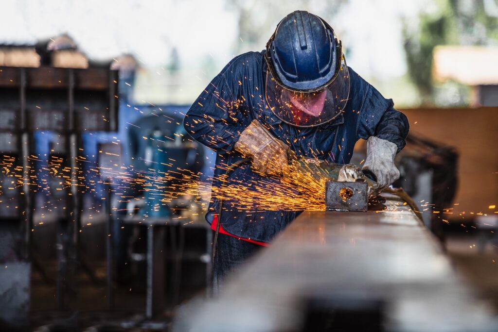Worker using electric wheel grinding on steel structure in factory