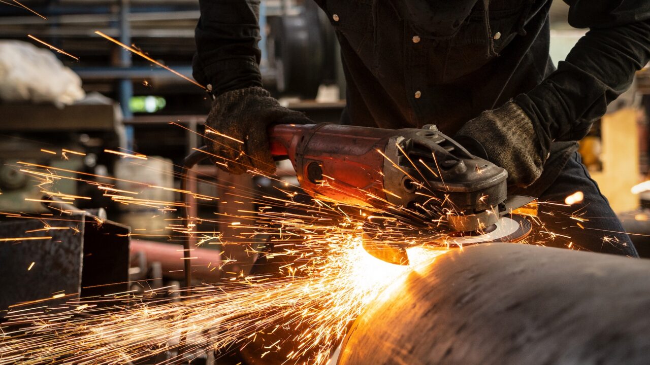 Close up of industrial worker using griding tool on a pipe with sparks flying.