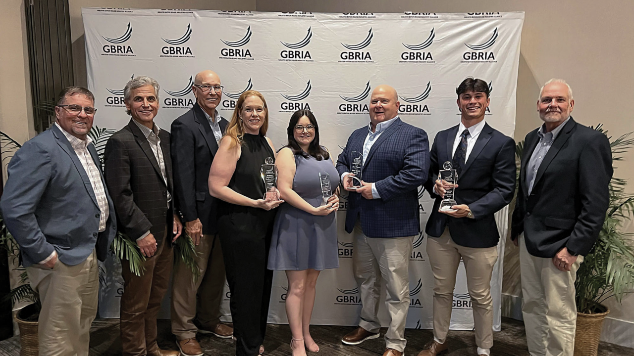 Eight people standing in a row in front of a GBRIA logo backdrop, with three holding glass awards.