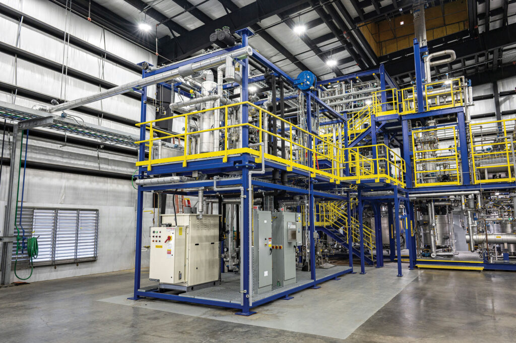 A large, multi-level industrial processing plant with blue steel scaffolding and yellow safety railings inside a warehouse.