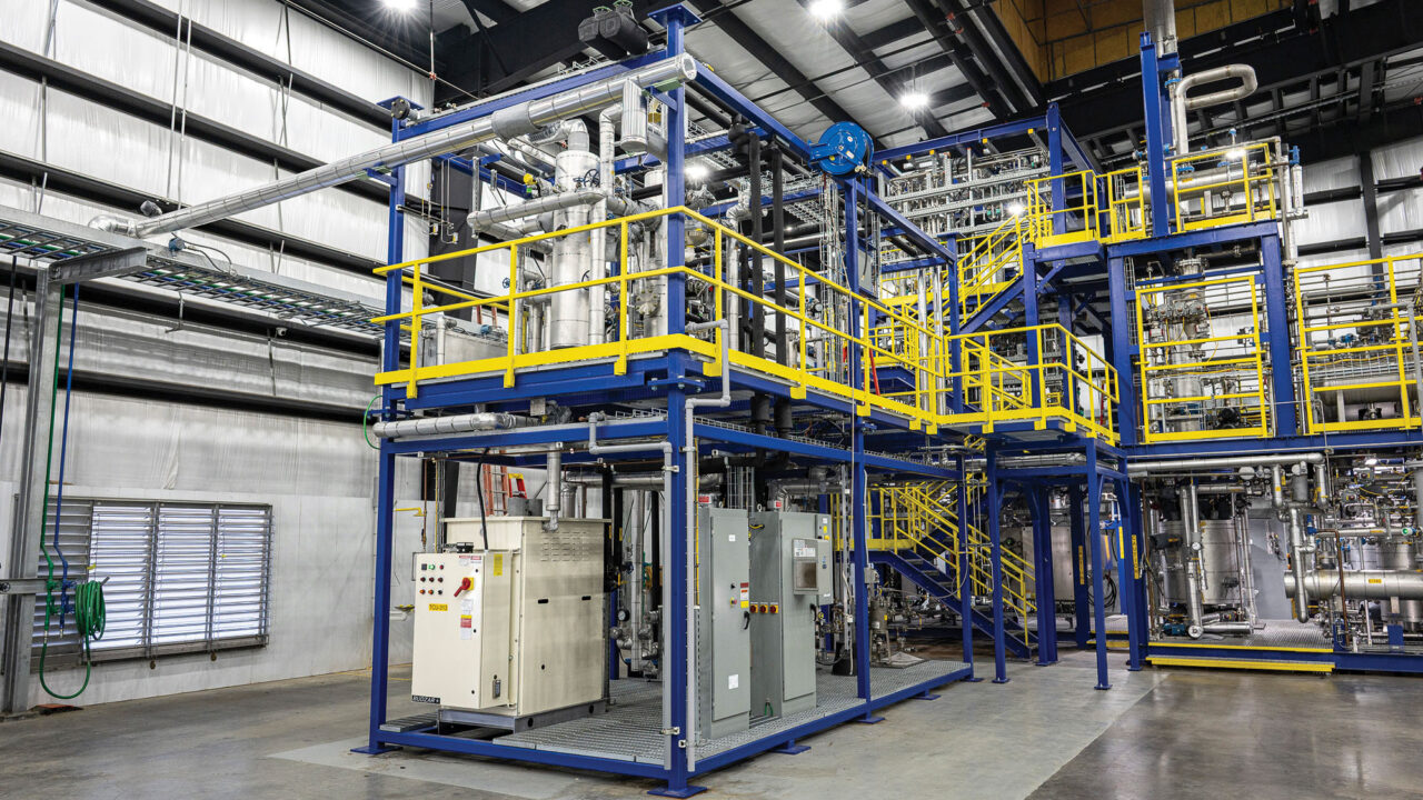 A large, multi-level industrial processing plant with blue steel scaffolding and yellow safety railings inside a warehouse.